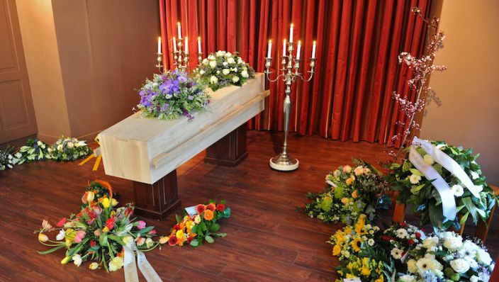 Свещи, ковчег и букети с цветя в червена атмосфера/Candles, coffin and flowers in a room with red atmosphere.